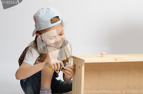 Image of Little girl in overalls collector of furniture screws screwdriver screw