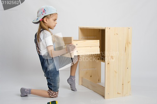 Image of Girl in overalls furniture assembler inserts a drawer chest of drawers