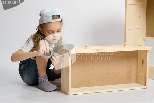 Image of Little girl in overalls collector of furniture making box on the dresser