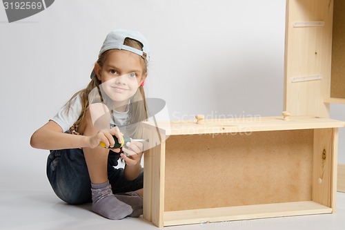 Image of Little girl in overalls collector collects furniture drawer of the dresser