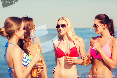 Image of group of smiling young women drinking on beach