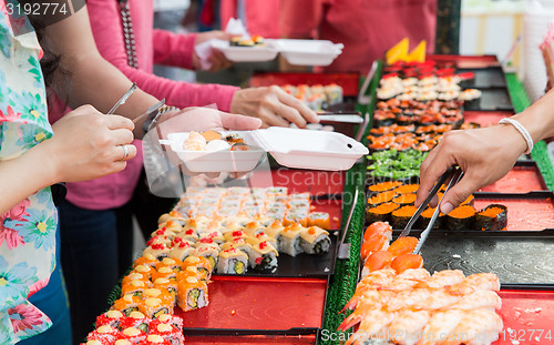 Image of close up of hands with tongs taking sushi