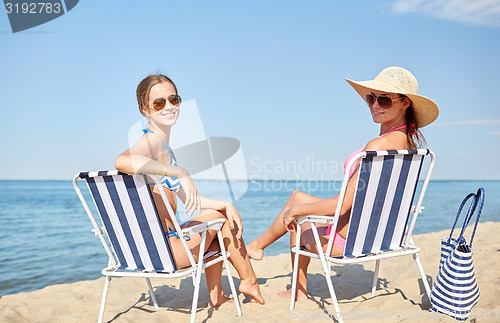 Image of happy women sunbathing in lounges on beach