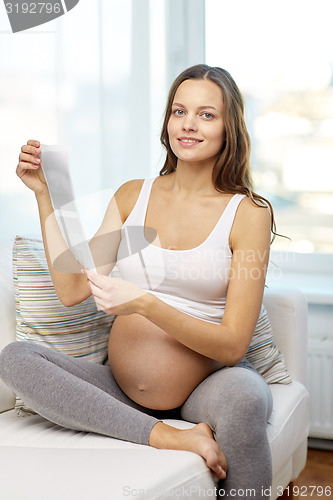 Image of happy pregnant woman with ultrasound image at home