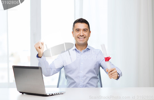 Image of smiling man with diploma and laptop at office