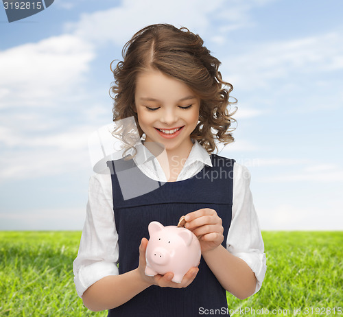 Image of happy girl putting coin into piggy bank