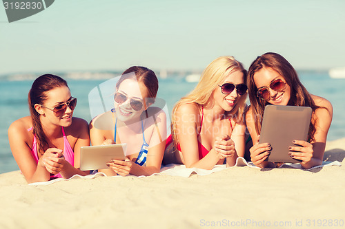 Image of group of smiling young women with tablets on beach