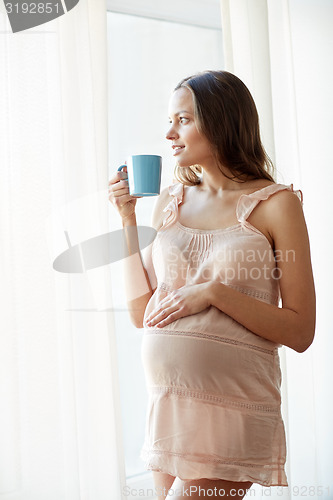 Image of happy pregnant woman with cup drinking tea at home