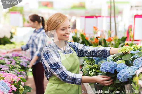 Image of happy woman taking care of flowers in greenhouse