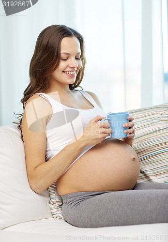 Image of happy pregnant woman with cup drinking tea at home