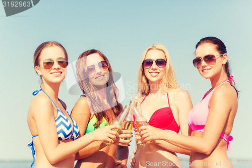 Image of group of smiling young women drinking on beach