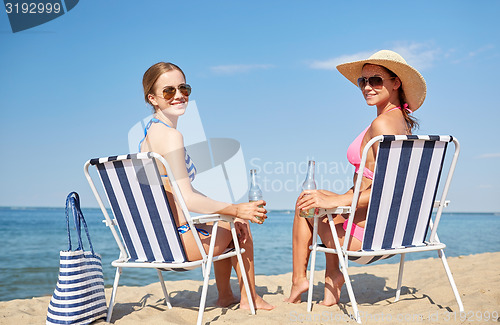 Image of happy women sunbathing in lounges on beach