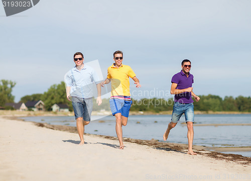 Image of smiling friends in sunglasses running along beach