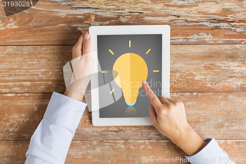 Image of close up of hands with lighting bulb on tablet pc