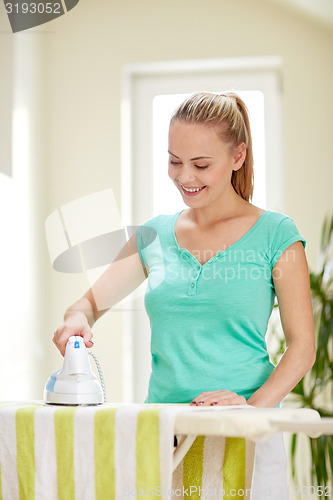 Image of happy woman with iron and ironing board at home