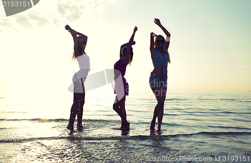Image of happy female friends dancing on beach