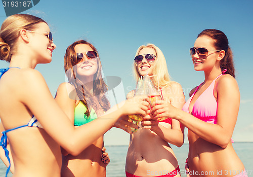 Image of group of smiling young women drinking on beach