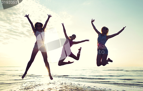 Image of happy female friends dancing and jumping on beach