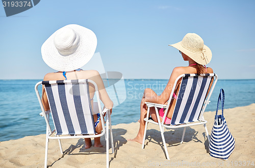 Image of happy women sunbathing in lounges on beach