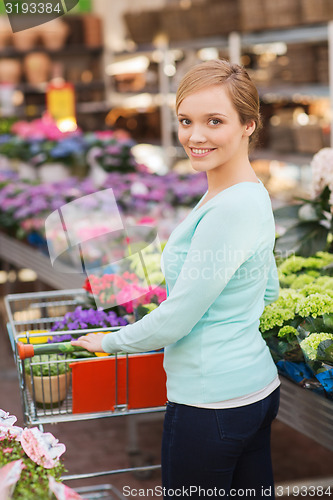 Image of happy woman with shopping trollye buying flowers