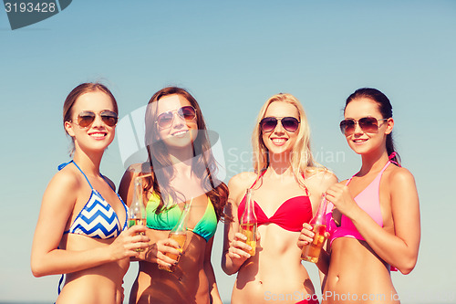 Image of group of smiling young women drinking on beach