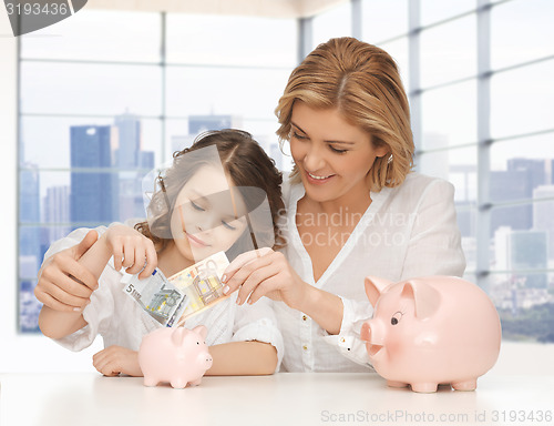 Image of mother and daughter putting money to piggy banks