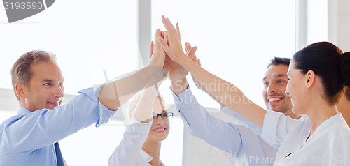 Image of happy business team giving high five in office