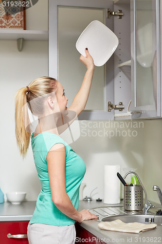 Image of happy woman putting plate to kitchen cabinet