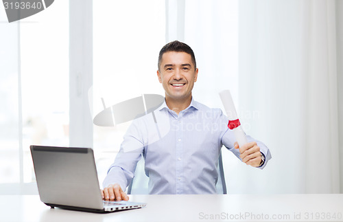 Image of smiling man with diploma and laptop at office