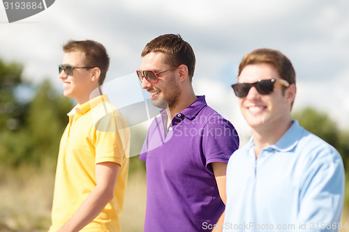 Image of smiling friends in sunglasses walking at summer