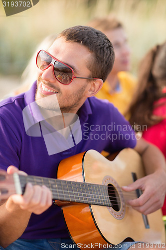 Image of group of happy friends playing guitar on beach