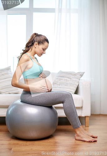 Image of happy pregnant woman exercising on fitball at home