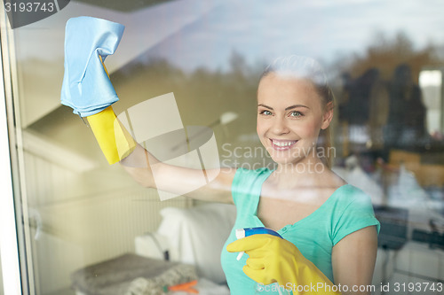 Image of happy woman in gloves cleaning window with rag