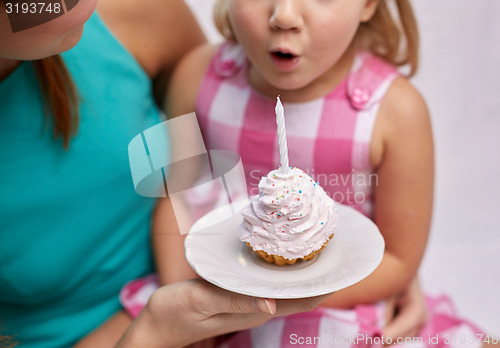 Image of happy mother and girl blowing out cupcake candle