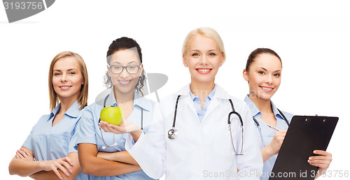 Image of smiling female doctor and nurses with green apple