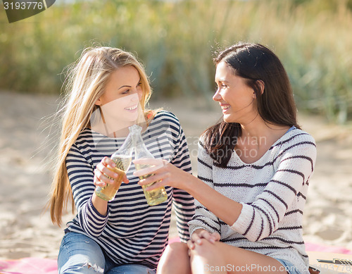 Image of happy young women drinking beer on beach