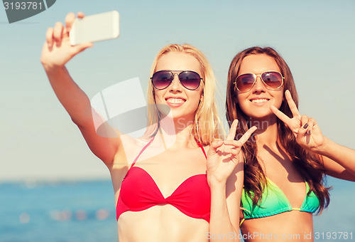 Image of two smiling women making selfie on beach