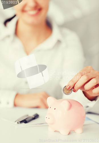 Image of woman hand putting coin into small piggy bank