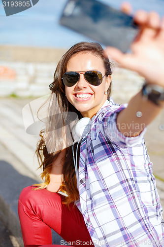 Image of smiling teenager taking picture with smartphone