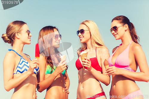 Image of group of smiling women eating ice cream on beach