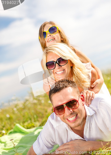 Image of smiling family in sunglasses lying on blanket