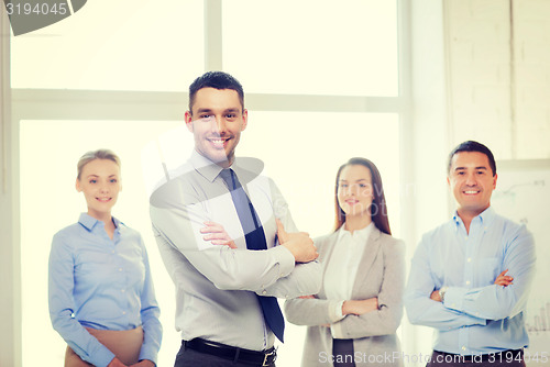 Image of smiling businessman in office with team on back