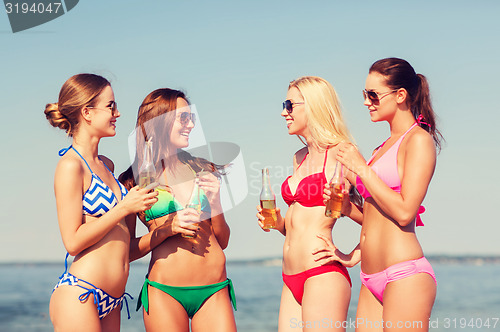 Image of group of smiling young women drinking on beach