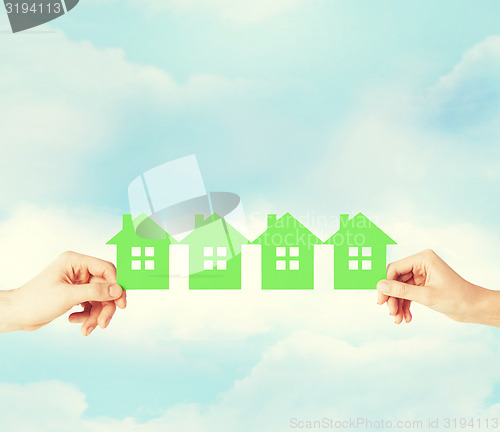 Image of man and woman hands with many green paper houses