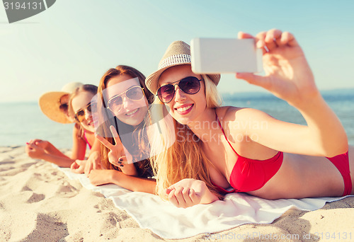 Image of group of smiling women with smartphone on beach