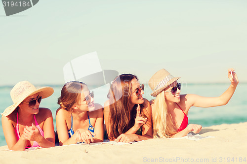 Image of group of smiling women with smartphone on beach