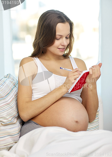 Image of happy pregnant woman writing to notebook at home