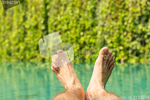 Image of close up of male feet over resort swimming pool