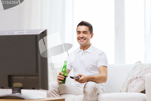 Image of smiling man watching tv and drinking beer at home