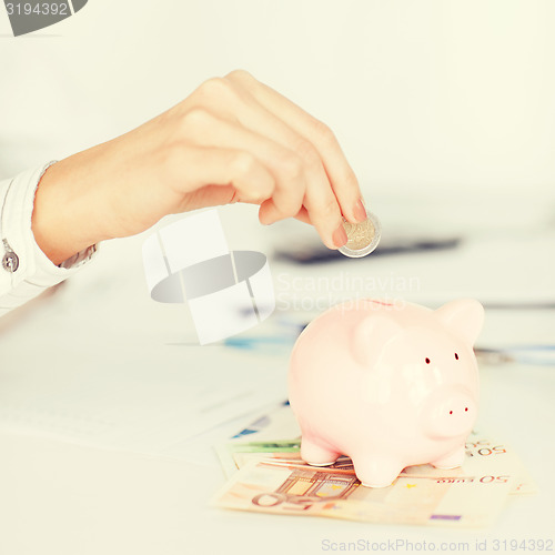 Image of woman hand putting coin into small piggy bank